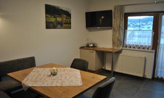 A cozy dining area with a wooden table and chairs. A picture of a landscape hangs on the wall, and a television is also present.