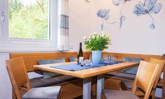 An inviting dining area with a wooden table and chairs. On the table are a bottle of wine and a vase with fresh flowers.