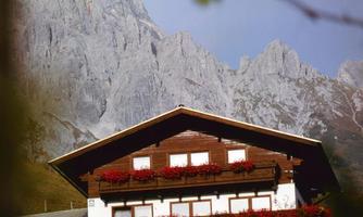 A traditional mountain house with blooming balconies. Majestic mountains rise in the background.