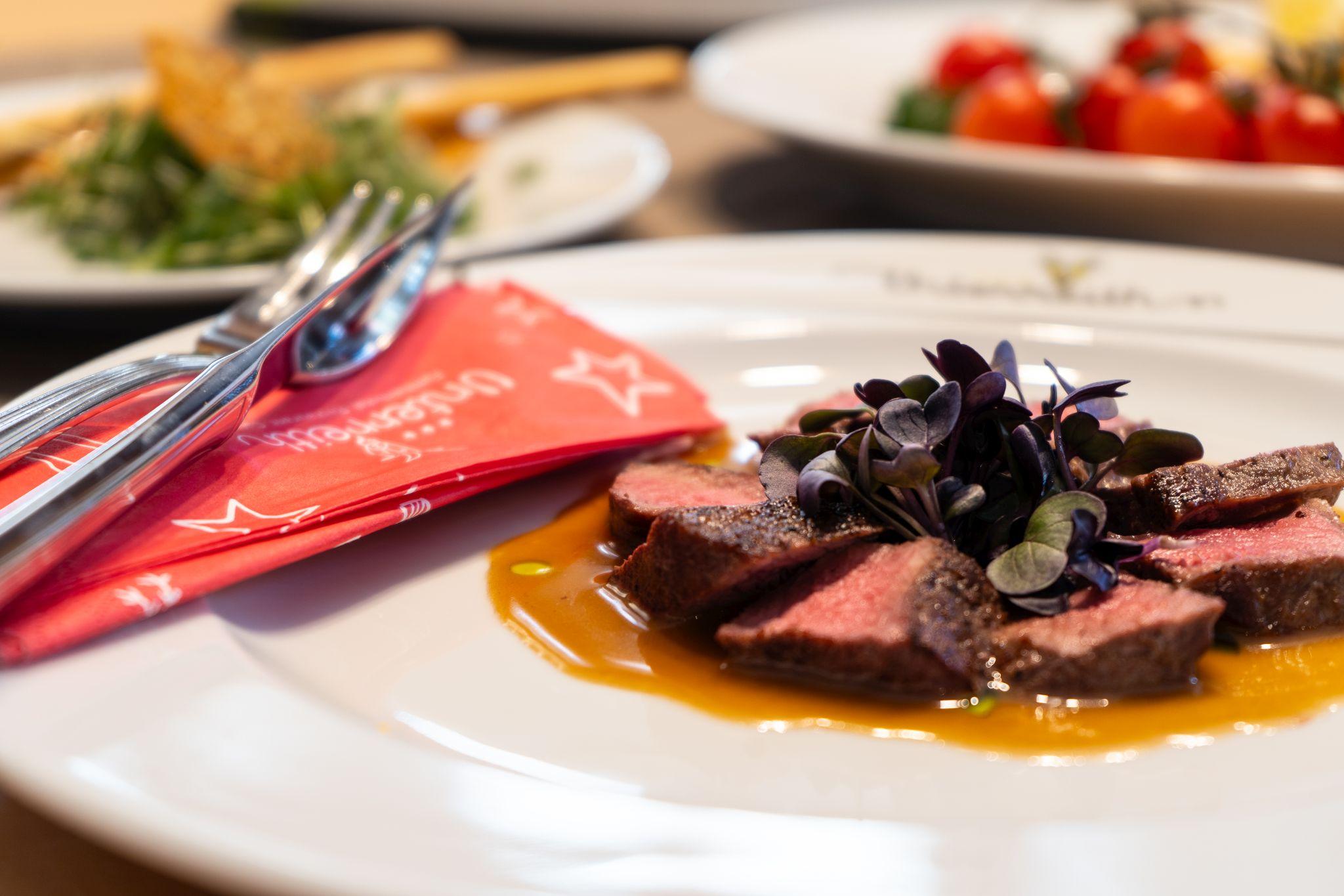 A delicious dish with tender meat, served on a white plate. In the background, fresh salads and other side dishes can be seen.