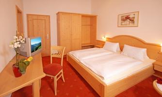 A cozy bedroom with a large double bed and a wooden desk. The room is bright and cheerful, with a TV and nice decoration.