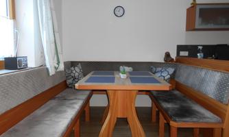 A cozy dining area with a wooden bench and a table. The walls are light, and there are some decorative elements hanging on the wall.