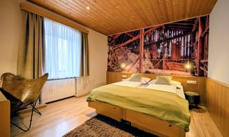 A cozy bedroom with a large bed and wooden ceiling. On the wall, there is an impressive picture of a wooden structure.