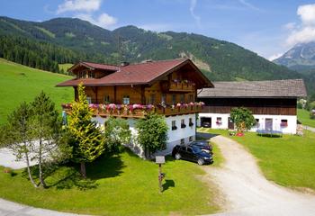 A picturesque chalet surrounded by green meadows and mountains. The sunny landscape conveys a cozy atmosphere.
