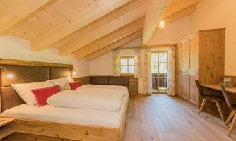 A cozy bedroom with wooden ceilings and two beds. Large windows provide a view outside and ensure plenty of daylight.