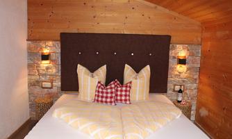 A cozy bedroom with a large bed and a wooden headboard. The pillows are colorful and the walls are made of stone, creating a warm atmosphere.