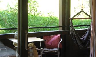 A cozy balcony with a table and chairs as well as a hammock. The view shows green grass and plenty of natural light.