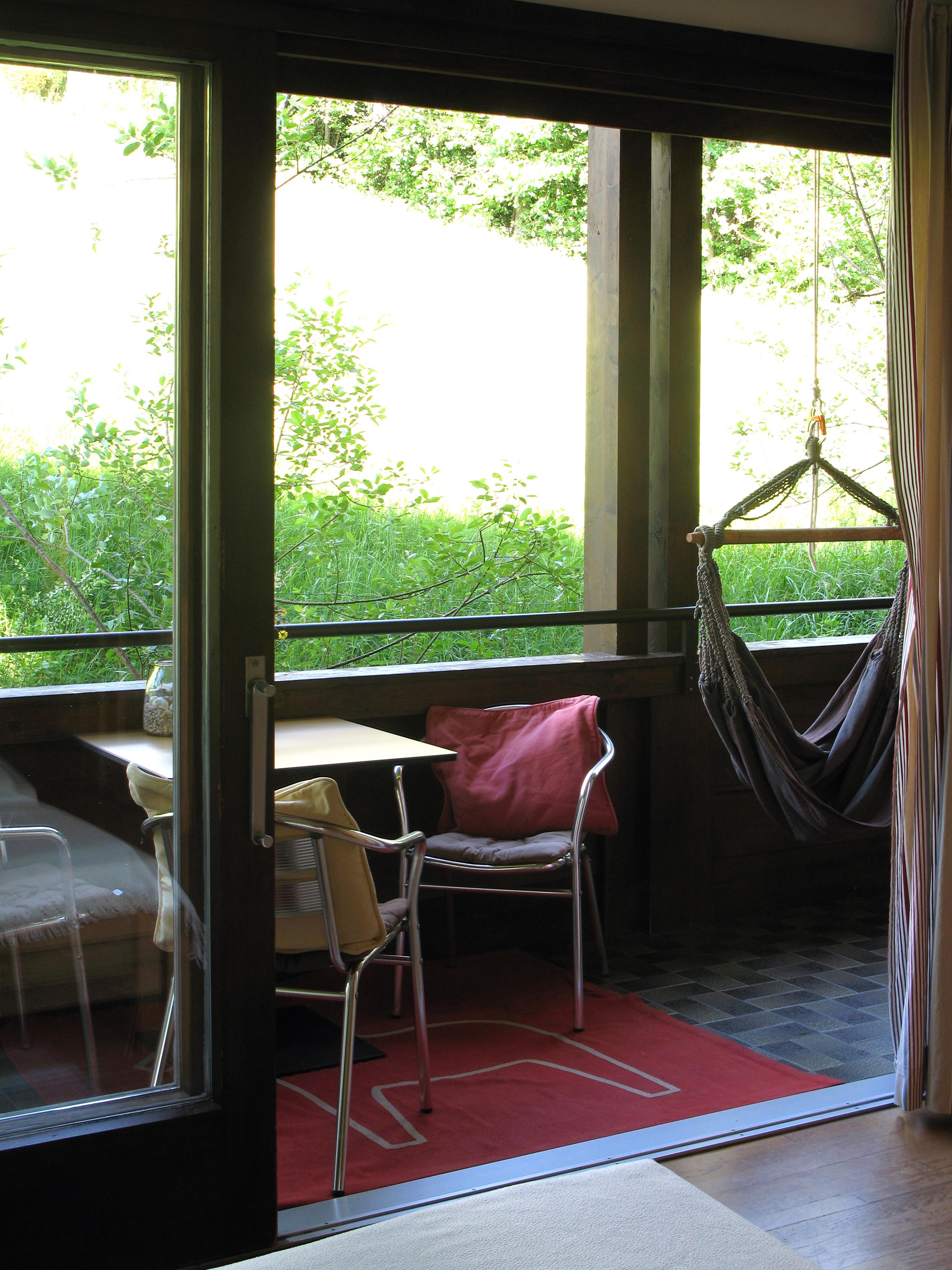 A cozy balcony with a table and chairs as well as a hammock. The view shows green grass and plenty of natural light.