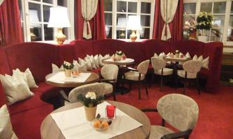 A cozy interior with red walls and comfortable seating. The tables are adorned with small plants and decorations.