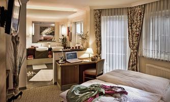 A cozy hotel room with two beds and a desk. In the background, there is a bathroom with a bathtub and beautiful decor.