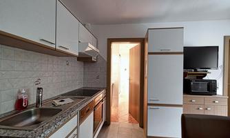 A modern kitchen with white cabinets and a granite countertop. In the background, a door and a television are visible.