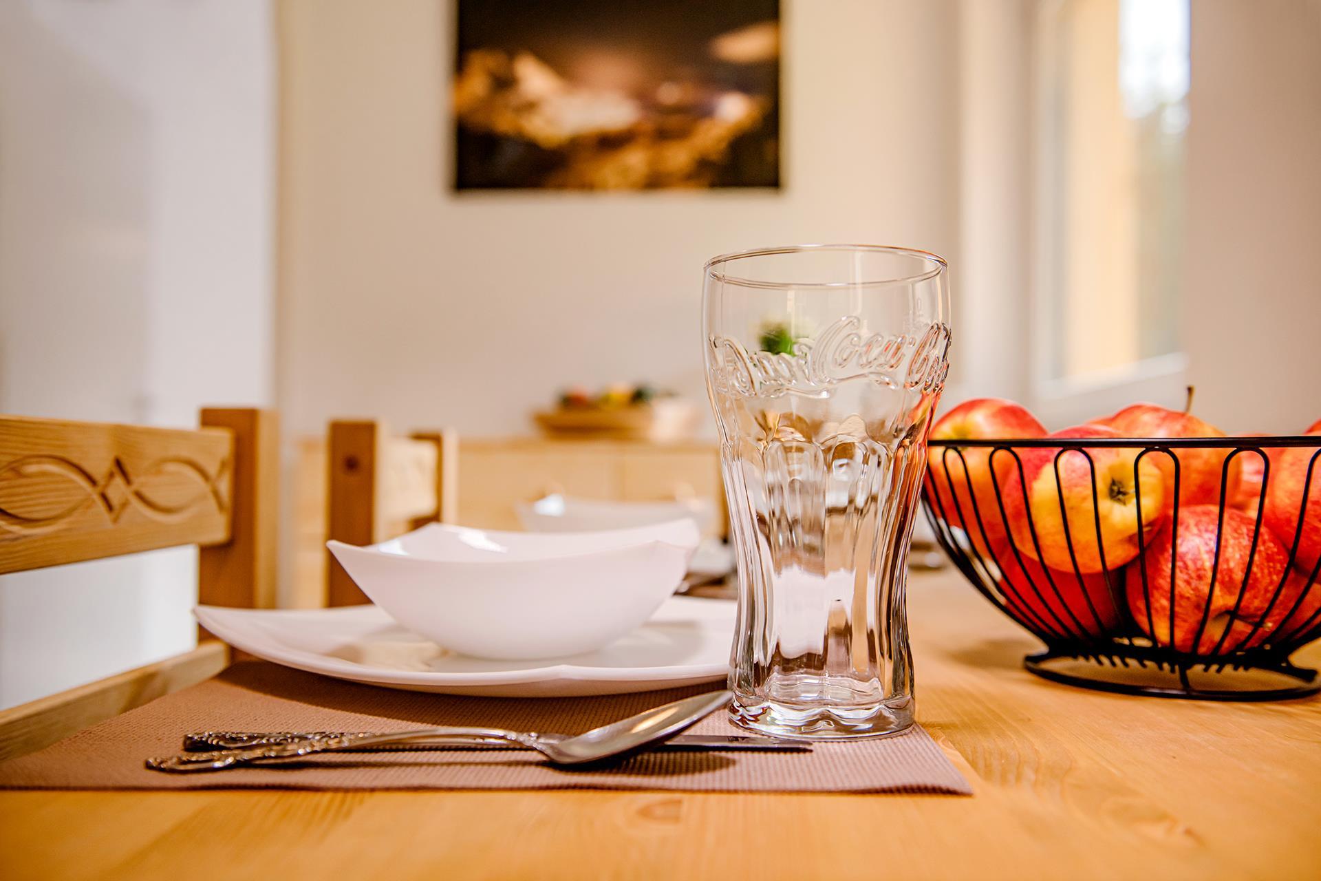 A set table with a glass, a white bowl, and cutlery. In the background, there is a bowl of apples.