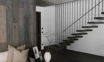 A modern living room with a minimalist staircase. The walls are made of wood and the furniture is in neutral colors.