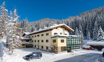 A snow-covered hotel in the mountains under a clear blue sky. Surrounded by tall, snow-covered fir trees.