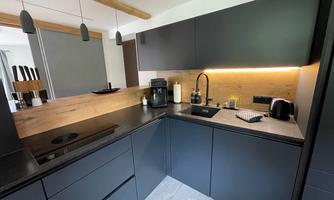 Modern kitchen with dark furniture and wooden details. Well-equipped workspace with coffee machine and sink.