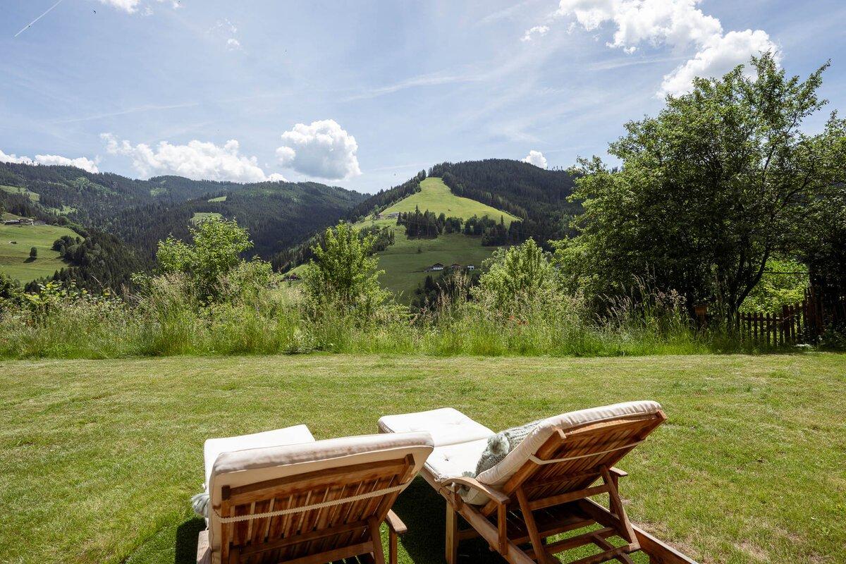 A picturesque landscape with gentle hills and lots of greenery. Two loungers are on a meadow overlooking the mountains.