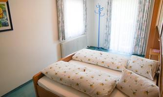 A cozy bedroom with a large double bed and comfortable pillows. Large windows let in plenty of daylight and create a bright atmosphere.