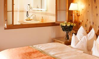 A cozy bedroom with a large bed and wood paneling. In the background, a bathroom with a mirror can be seen.