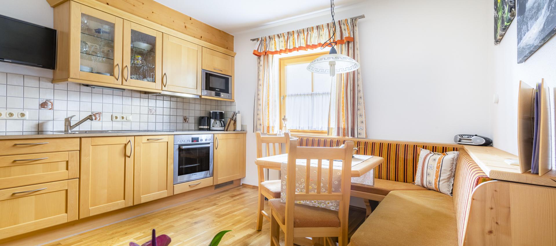 A modern kitchen with wooden cabinets and a cozy dining area. Light falls through a window, creating an inviting atmosphere.