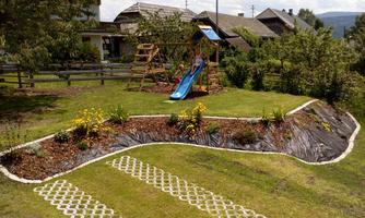 A well-maintained garden with a slide playground and colorful flowers. In the background, several buildings and trees are visible.