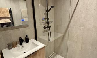 A modern bathroom with a stylish shower and a wooden sink. The walls are painted in neutral colors, and there are toiletries visible on the shelf.