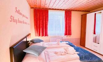 A cozy bedroom with two beds, wooden ceiling, and red curtains. On the wall, there is an inspiring quote.