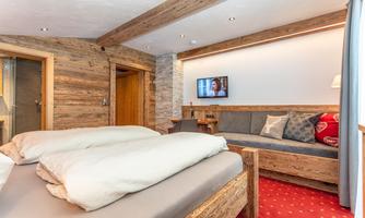 A cozy room with a double bed and a living area. On the wall, there is a television and the furniture is made of wood.