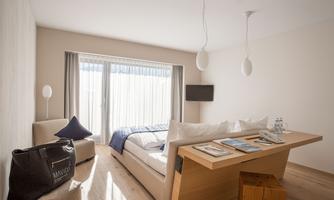 A modern room with a comfortable bed and large windows. Bright colors and minimalist furniture create an inviting atmosphere.