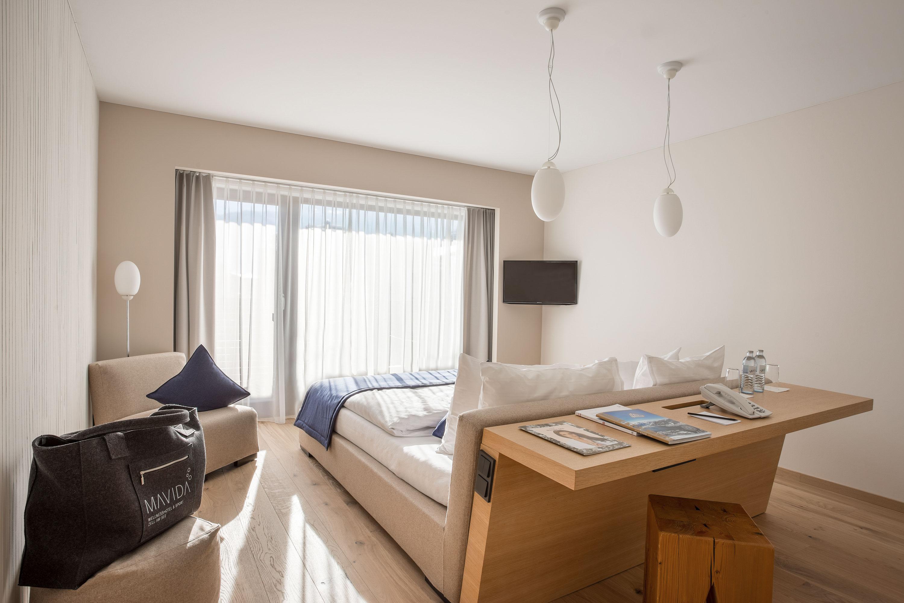 A modern room with a comfortable bed and large windows. Bright colors and minimalist furniture create an inviting atmosphere.