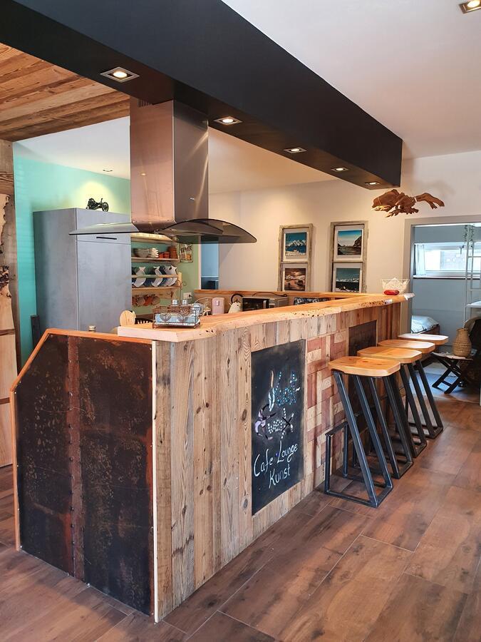 A modern kitchen corner with a wooden bar and stools. The wall is decorated with a black board for notes.
