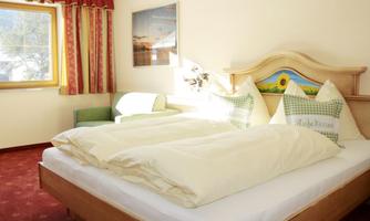 A cozy bedroom with a large bed covered with white bedspreads. The room features a chair and a window with a view outside.