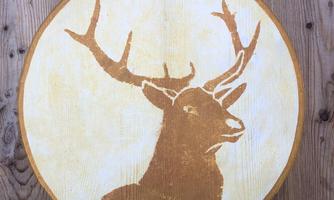 A stylized image of a stag's head in a large, circular frame. The background consists of wood in a warm tone.