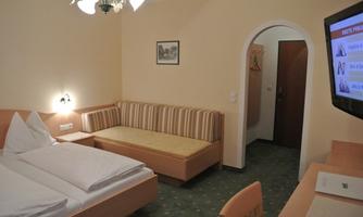 A simple hotel room with two single beds, a sofa, and a television. The walls are painted in a soft yellow tone.
