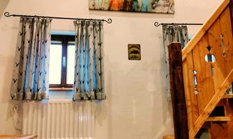 A cozy entrance area with wooden floorboards and a staircase. A colorful painting of a deer hangs on the wall, and the windows are decorated with light curtains.