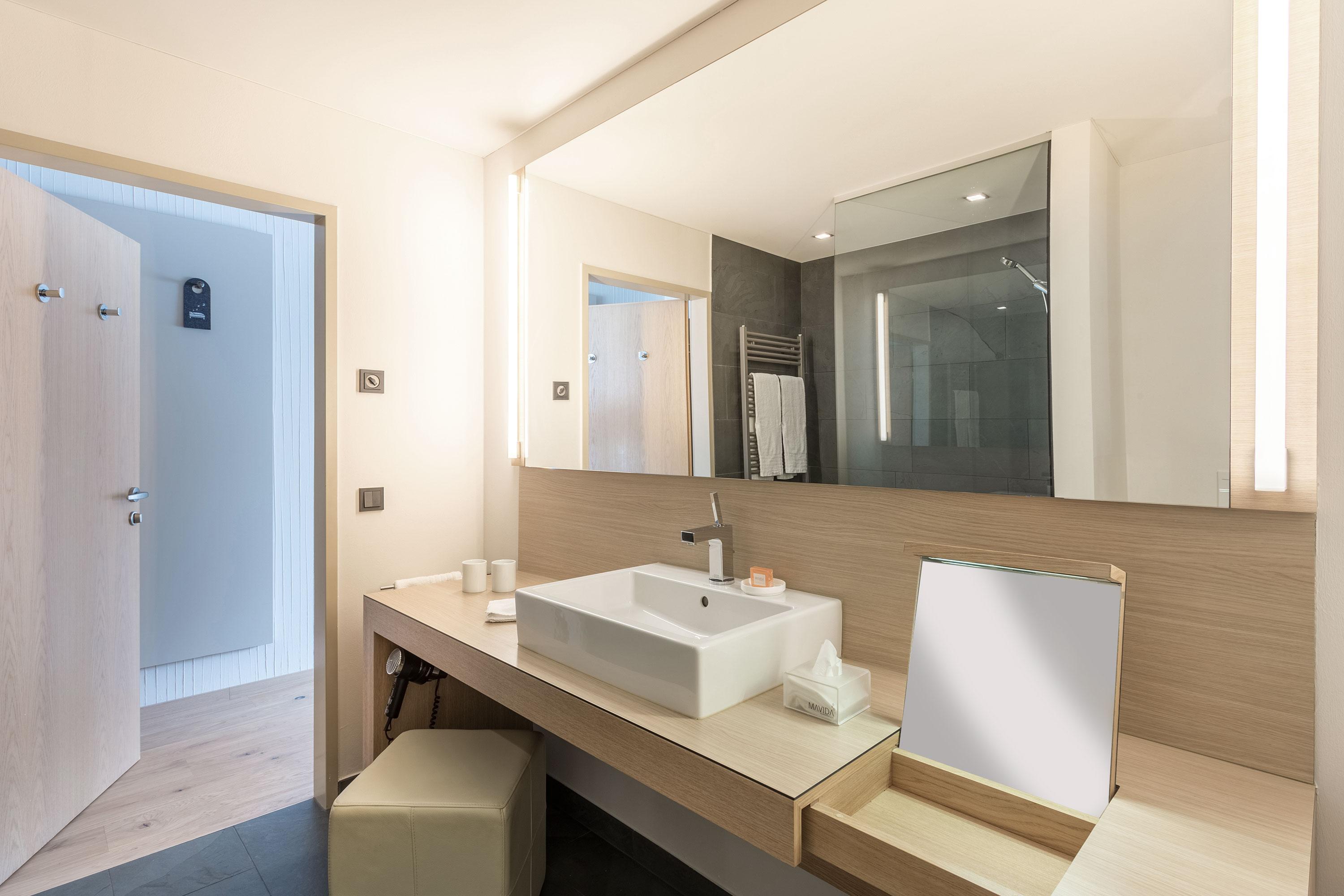 A modern bathroom with a white sink and large mirrors. The walls are bright and the lighting is pleasant.