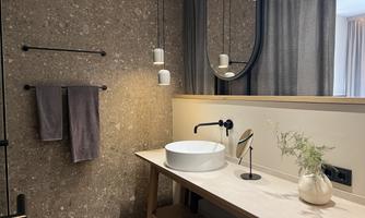 A modern bathroom with a stylish wooden vanity top. The walls are adorned with a natural stone pattern, and there is elegant mirror lighting.