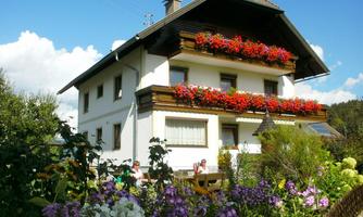 A beautiful house with flower balconies and colorful flowers in the foreground. The surroundings are green and inviting.