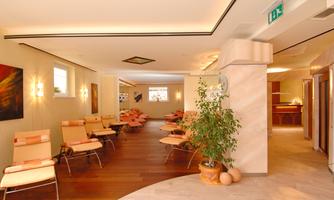 A modern waiting room with comfortable armchairs and a warm wooden floor. Soft lighting creates a relaxed atmosphere.
