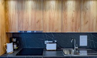 A modern kitchen with wooden cabinets and a dark stone floor. The amenities include a stove, a sink, and a microwave.