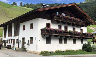 A traditional house with a wooden porch and flowering boxes. It is located in a green hillside landscape.