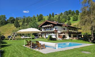 A beautiful property with a pool and sun loungers in a green environment. In the background, mountains and a blue sky can be seen.