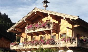 A traditional wooden house with blooming balcony boxes. The facade is adorned with flowers and the surroundings are surrounded by nature.
