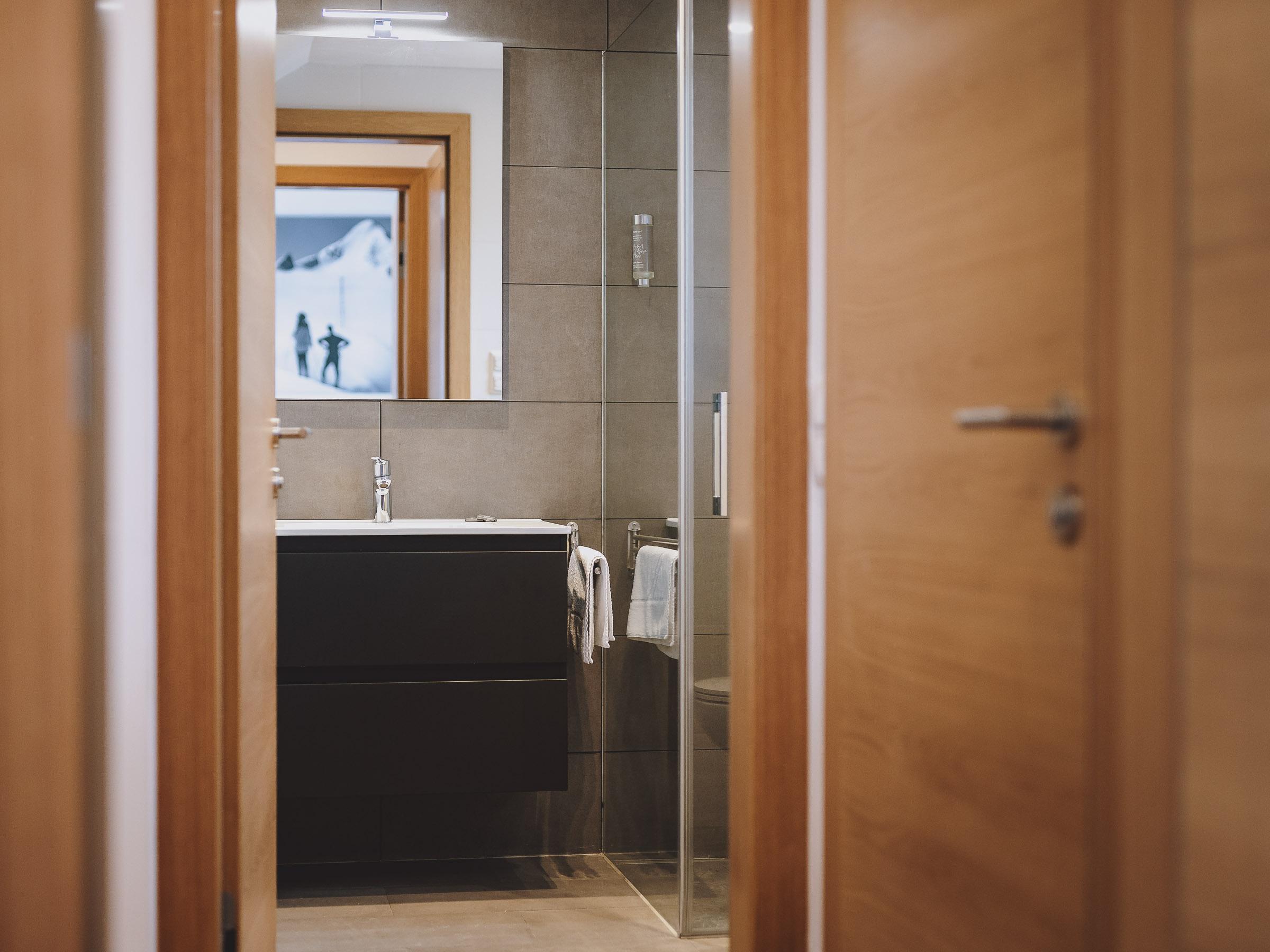 A modern bathroom with an elegant shower and a stylish sink. The walls are in neutral colors and the doors are made of wood.