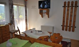 A cozy room with two beds, a television, and a table. The walls are made of wood, and there are large windows with a view outside.
