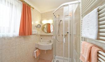 A modern bathroom with a shower and wall tiles. Large windows provide plenty of daylight.