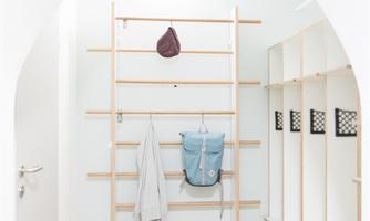 A modern entryway with a light wood floor. On the wall, there is a minimally designed shelf with clothes and a bag.