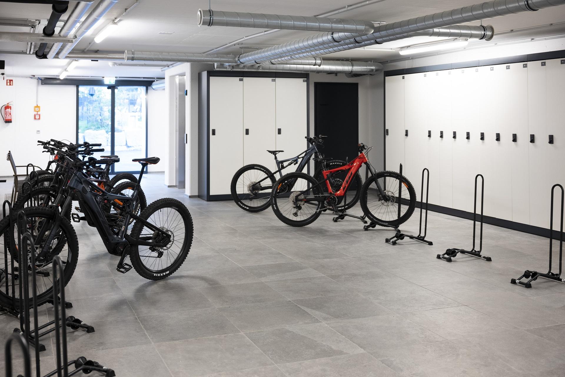 A modern bike room with multiple bicycles and bike racks. The walls are light, and there are lockers for storage.