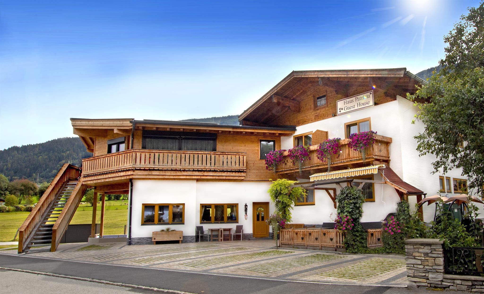 A beautiful alpine building with wooden cladding and a balcony. Blooming plants and a picturesque landscape surround the house.