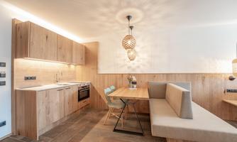 A modern kitchen with wooden shelves and an inviting dining area. The room is bright and welcoming with stylish lighting elements.
