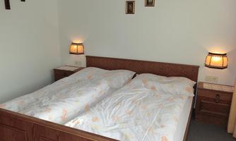 A cozy bedroom with a double bed and two nightstands. The walls are plain and there is soft lighting.
